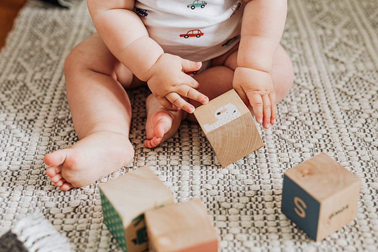 services-04 A baby sitting and playing with wooden toy blocks on a textured carpet indoors.