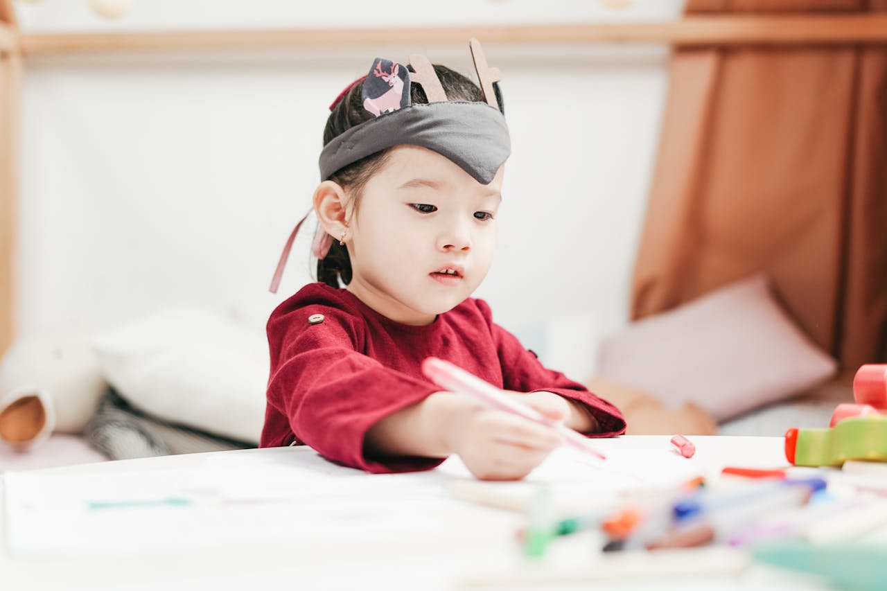 gallery-05 A young child wearing a headpiece enjoying drawing in an indoor playroom setting.